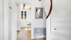 Un interior blanco con una escalera de madera, un escritorio y una silla en un pasillo.