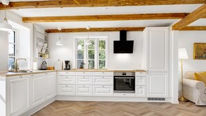 Una cocina moderna con armarios blancos, suelo de madera en espiga y vigas de madera a la vista.