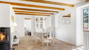 Una sala de estar moderna con chimenea, vigas de madera, un comedor con sillas blancas y un patrón de suelo en espiga.
