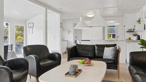 Un soggiorno moderno con un tavolino da caffè bianco, divani in pelle nera e un angolo cottura con pensili bianchi e illuminazione a sospensione.