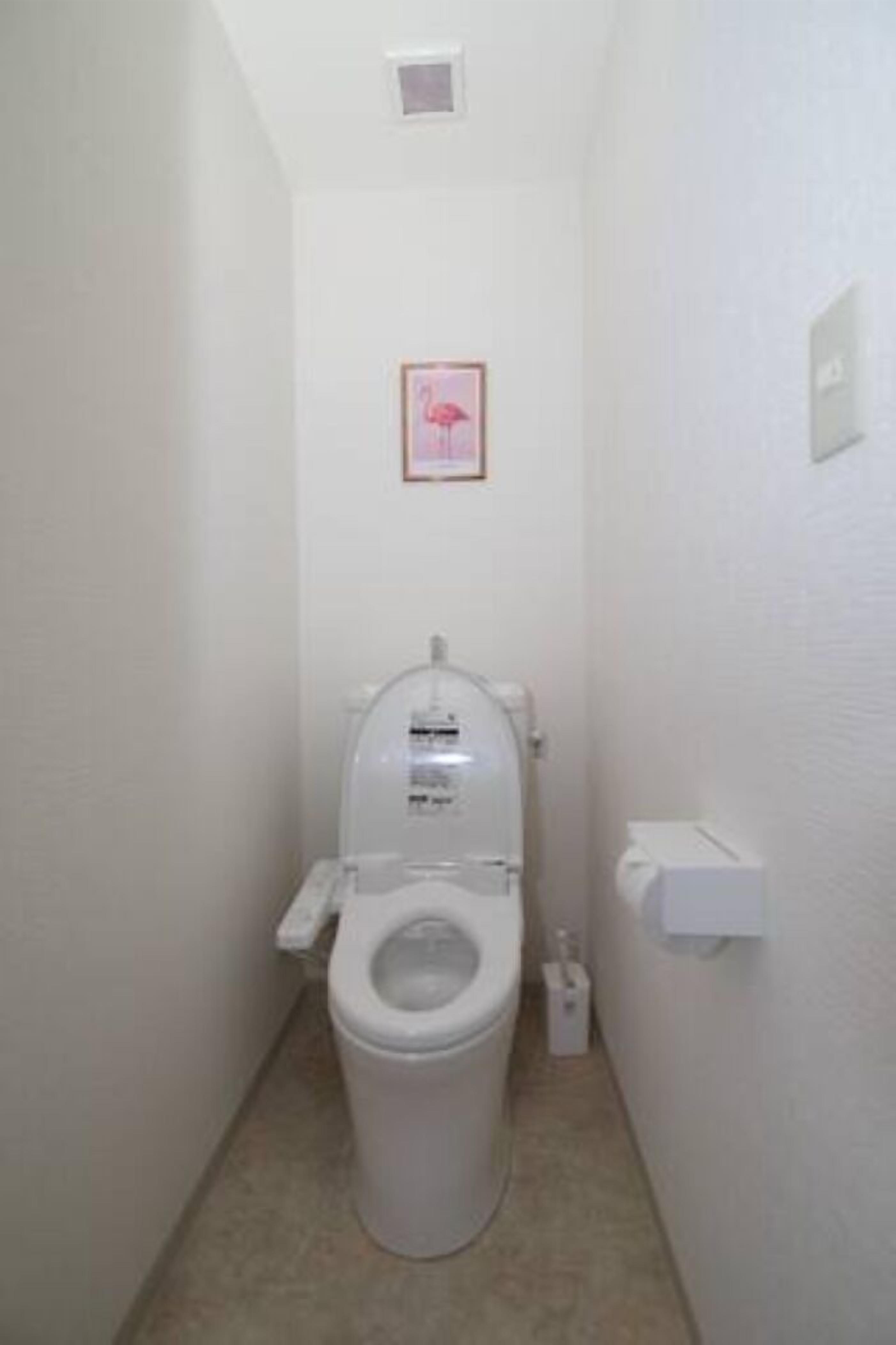 A small, white bathroom with a toilet, a trash bin, and a framed picture on the wall.