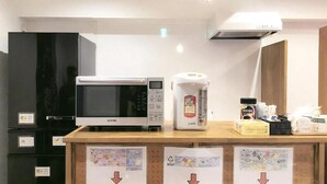 A kitchen area with a microwave, a coffee maker, and a refrigerator. There are signs with arrows pointing downwards on the counter. - Guest House Siesta (Tokyo)