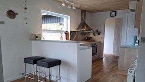A modern kitchen with a central island, two bar stools, a window, and a view of the outside. - "Falk" - 900m from the sea by Interhome (Skagen)