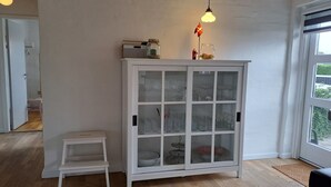 A room with a white cabinet with glass doors, a small white stool, and a hanging light fixture. - "Falk" - 900m from the sea by Interhome (Skagen)