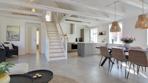 A spacious living area with a staircase, a dining area with wicker chairs, and a kitchen with a large island.