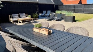 An outdoor patio area with a wooden table, wicker chairs, and lounge chairs.