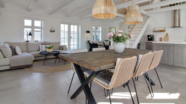 A spacious living area with a large wooden dining table, wicker chairs, and hanging pendant lights.