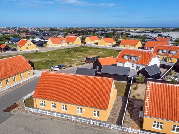 Zona residencial con casas de techos anaranjados y paredes amarillas, dispuestas en un patrón de cuadrícula, con una vista despejada al mar en el fondo.