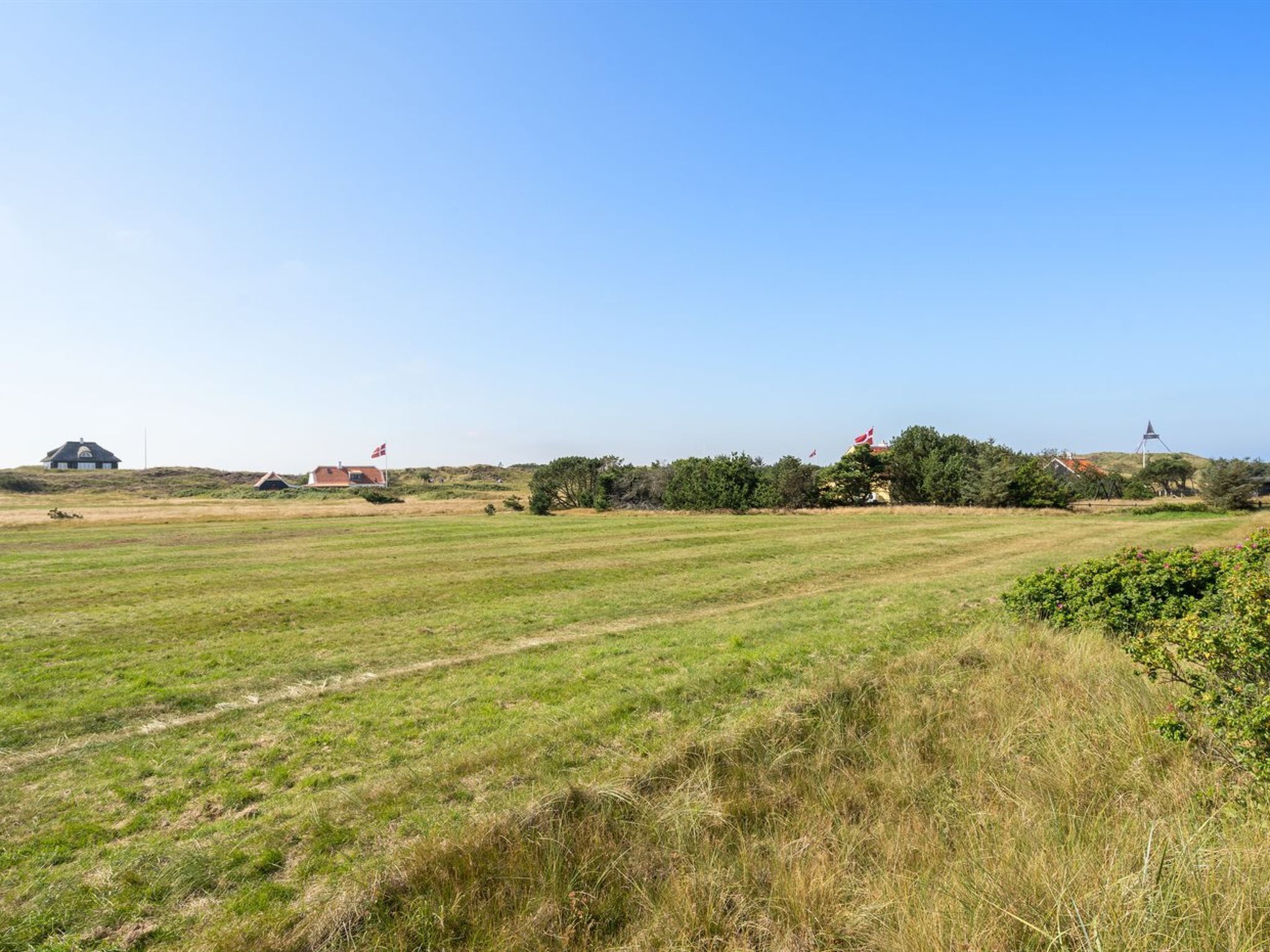 A rural landscape with a large open field, a few buildings, and a windmill in the distance.