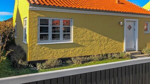 Een geel huis met een rode dakbedekking, witte ramen en een deur.