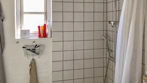 Een badkamer met een douche, een raam en een plank met toiletartikelen.