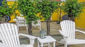 Een terras met witte Adirondack-stoelen, een tafeltje met een lantaarn en een potplant.