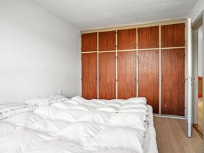 Un dormitorio con un amplio armario de madera, una cama con ropa de cama blanca y un techo blanco.