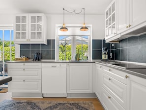 A modern kitchen with white cabinetry, a built-in dishwasher, a coffee maker, and a window with a view of greenery.