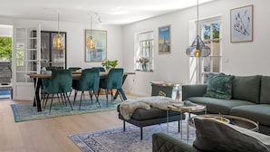 Una sala de estar moderna con un sofá, un comedor con sillas, y una cocina visible a través de una puerta abierta.