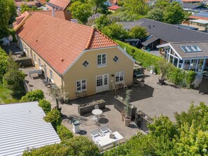Une maison à deux étages avec un toit recouvert de tuiles rouges, une cour dotée d’un espace salon extérieur et un jardin.