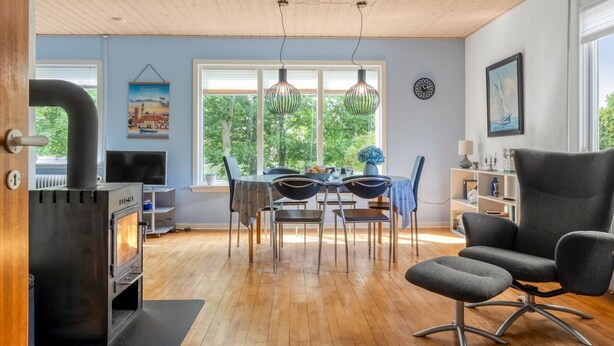 Een moderne woonkamer met een houtkachel, eethoek en een groot raam met uitzicht op groen.