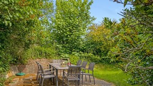 Een terras buiten met een stenen tafel en stoelen, omringd door weelderige begroeiing.
