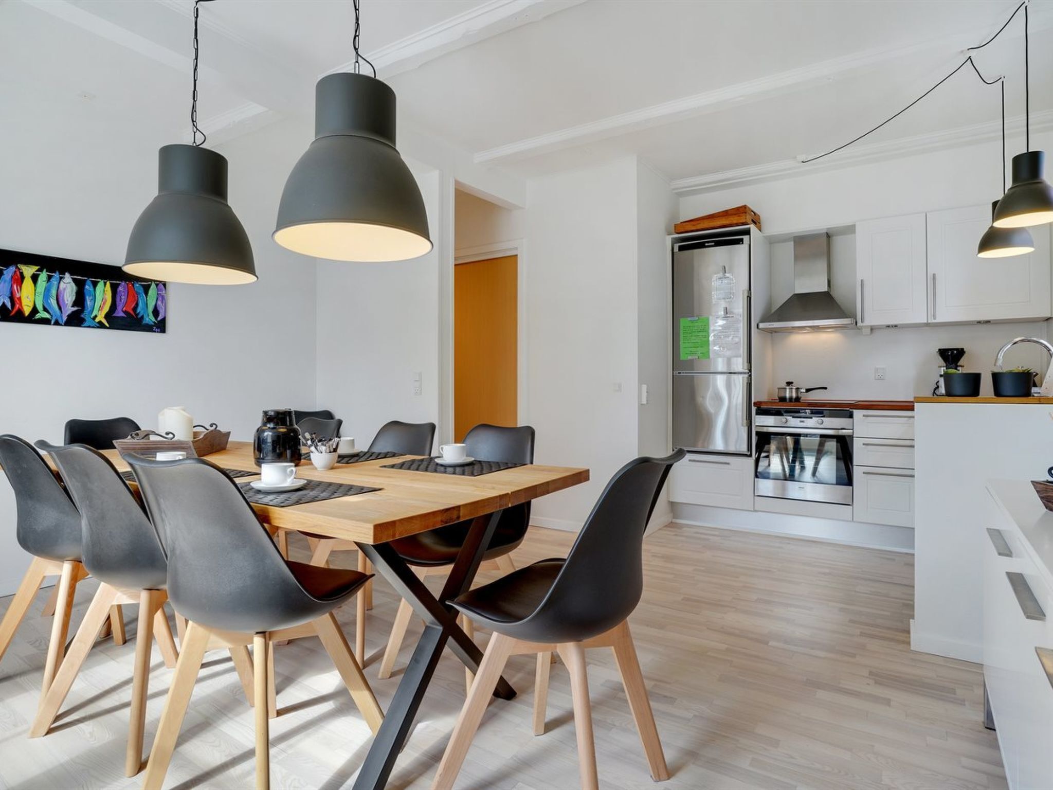 A modern kitchen with white cabinets, stainless steel appliances, and black pendant lighting.