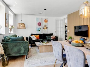 A modern living room with a green sofa, a coffee table, and a dining area with chairs and a TV.