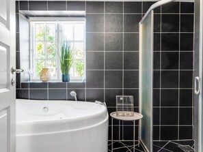 Ein modernes Badezimmer mit einer freistehenden Badewanne, einem Fenster mit Blick ins Grüne und einer Dusche mit schwarzen Fliesen.