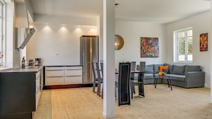 Una cocina moderna con refrigerador empotrado, un área de comedor con sofá gris y sillas negras, y piso de madera.