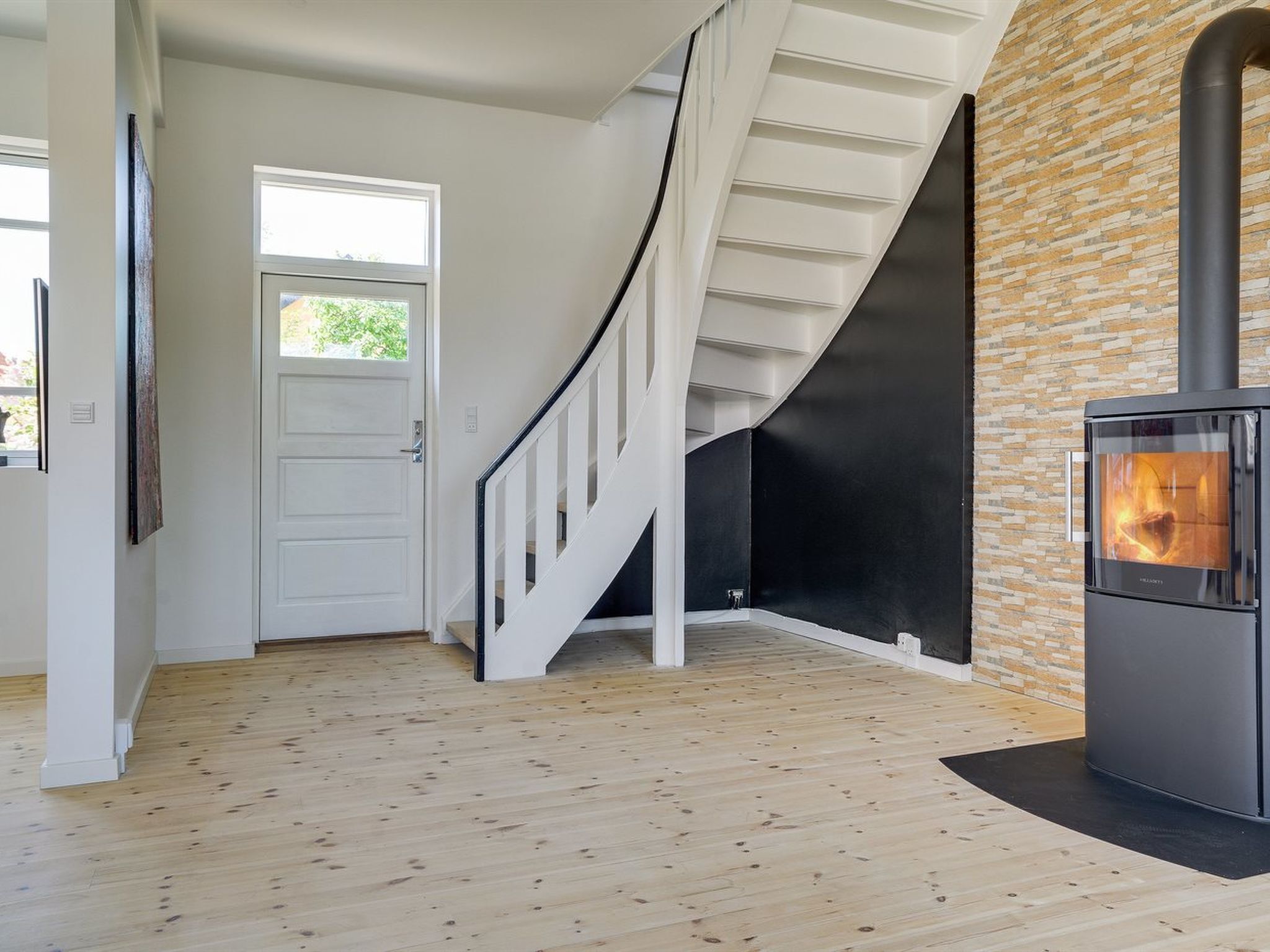 A modern interior with a wooden floor, a white staircase, a black wall, and a wood-burning stove.