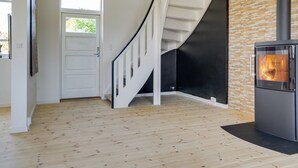 Un interior moderno con piso de madera, una escalera blanca, una pared negra y un estufa de leña.