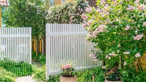 Un jardín con cerca blanca, plantas en macetas y un sendero.