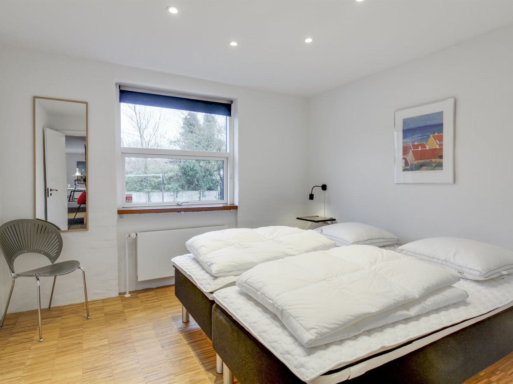 A modern bedroom with a bed, a chair, a window, and a picture on the wall.