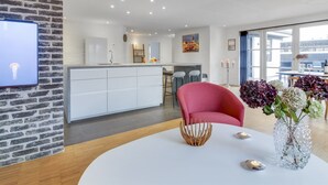 A modern kitchen with white cabinets, a central island, and a dining area with a round table and a red chair.