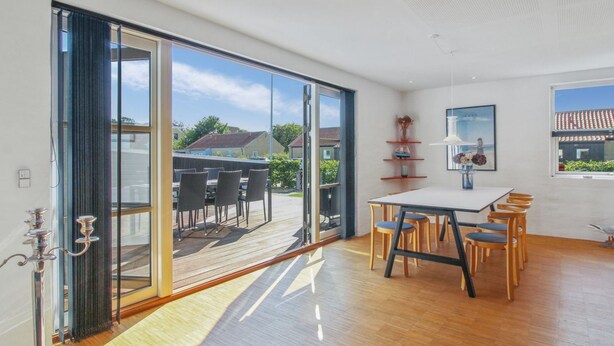 A spacious room with a large sliding glass door leading to an outdoor patio. Inside, there is a dining area with a table and chairs.