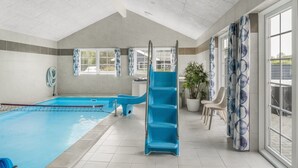 Una piscina con un tobogán azul, una zona de estar con sillas y ventanas grandes.