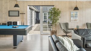 Una sala de estar moderna con una mesa de billar, un sofá y un sillón. Una puerta da acceso a un balcón con vistas.