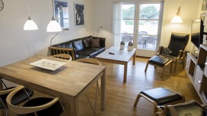 Een moderne woonkamer met een houten eettafel, een zwarte leren bank en een groot raam met uitzicht op het landschap.