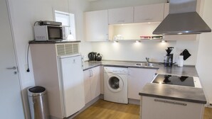 Een functionele keuken met een magnetron, wasmachine, spoelbak en een klein afvalbakje.