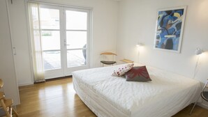 Een slaapkamer met een groot bed, een schuifdeur naar buiten, een stoel, een klein tafeltje en een wandlamp.