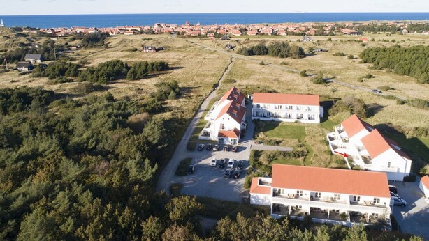 Luchtbeeld van een kustgebied met een groot wit gebouw met een rood dak, omringd door groen en een weg ernaartoe.
