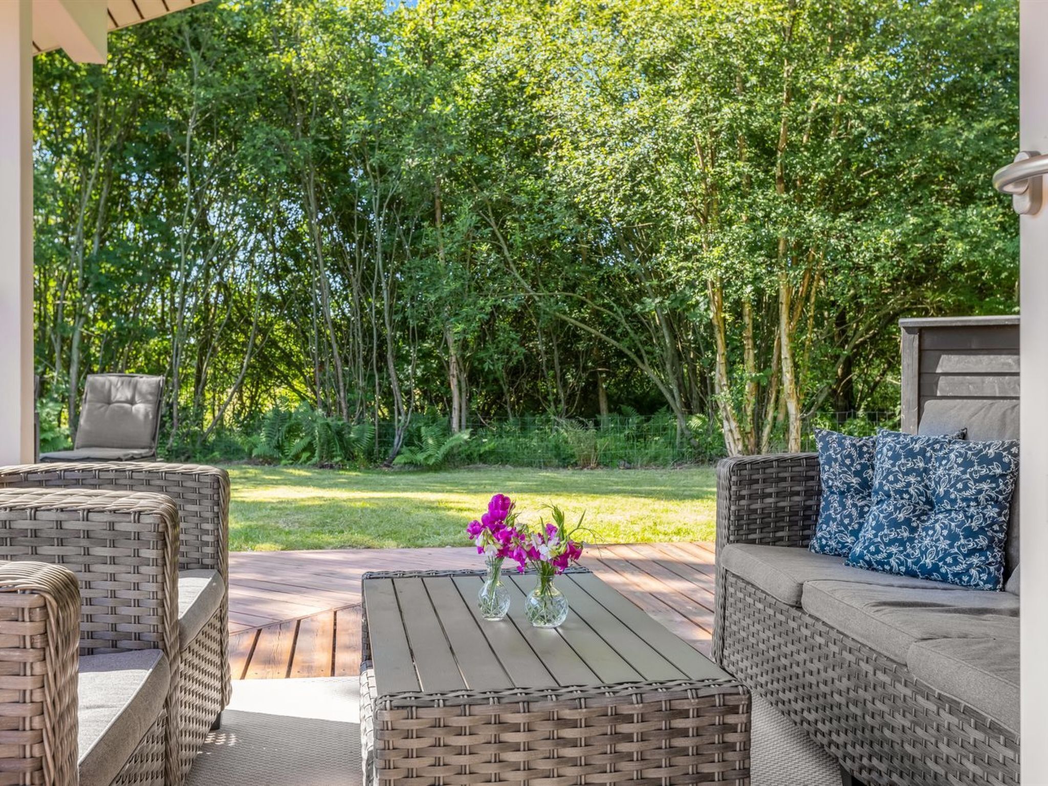 Eine Außenpatio mit Korbmöbeln, einem Tisch mit Blumenvase und Blick auf einen dichten Wald.