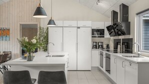 Una cocina moderna con armarios blancos, una isla central con taburetes de bar, una lámpara colgante y vistas al exterior a través de una ventana.