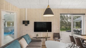 Una sala de estar moderna con un televisor de pantalla plana grande, un sofá, una mesa de centro y un comedor con sillas.