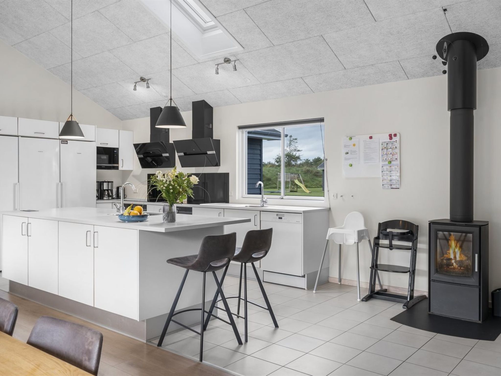 A modern kitchen with white cabinetry, a central island with bar stools, a black stove, and a large window offering a view of the outdoors.