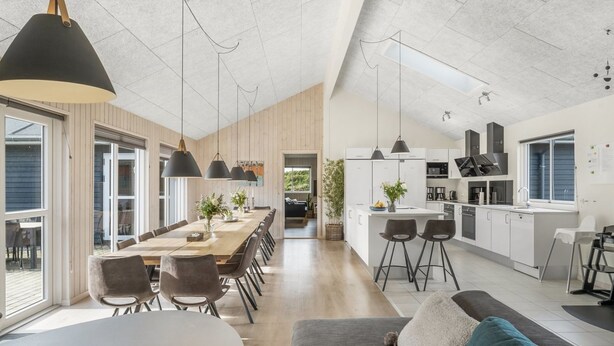 Una cocina moderna con armarios blancos, una zona de comedor con una mesa larga y sillas, y un rincón de estar acogedor con un sofá y una mesa de centro.