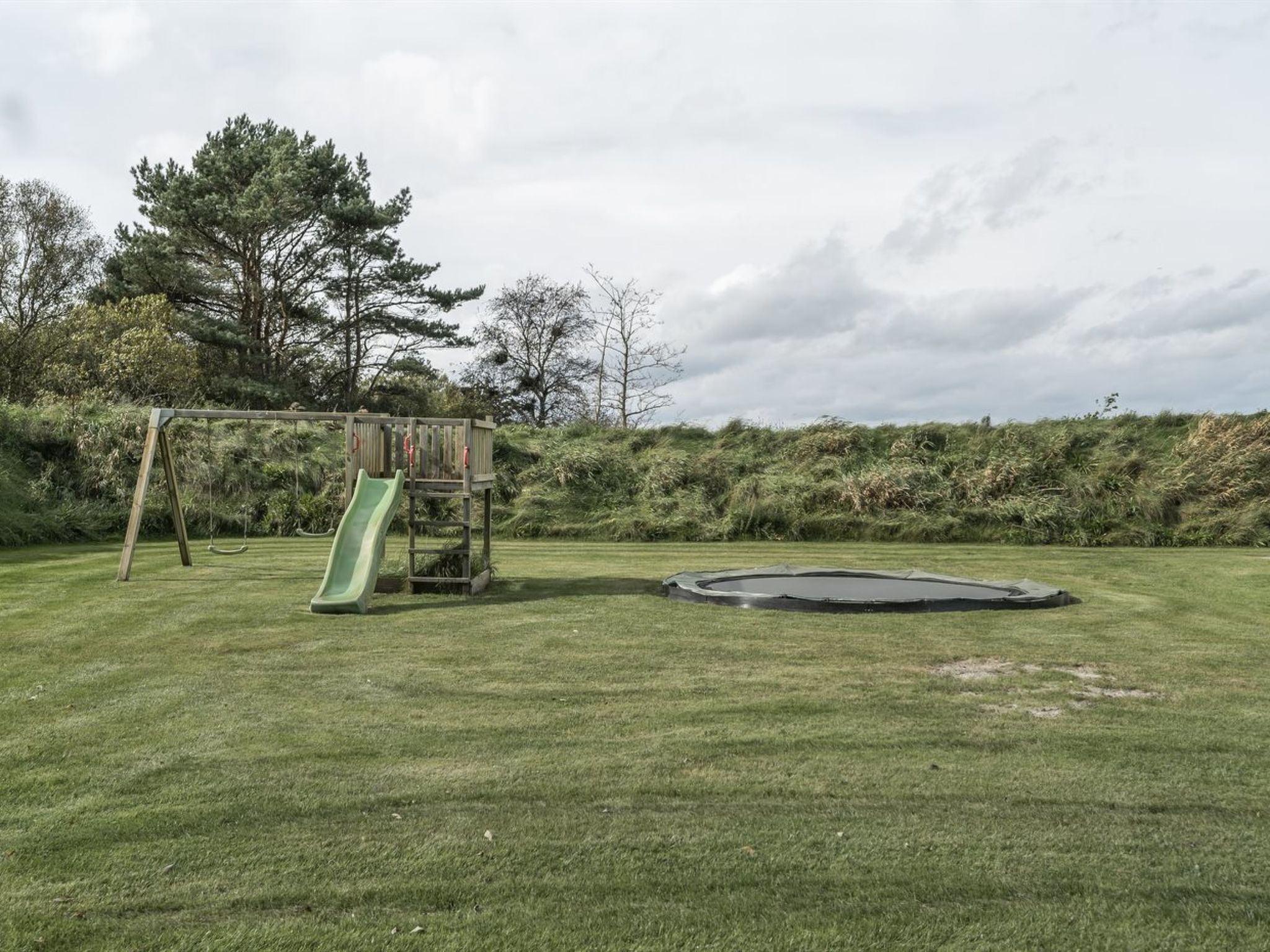 A grassy outdoor area with a wooden play structure, including a slide and a small climbing frame.
