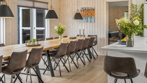 Un comedor moderno con una larga mesa de madera, múltiples sillas e iluminación colgante.