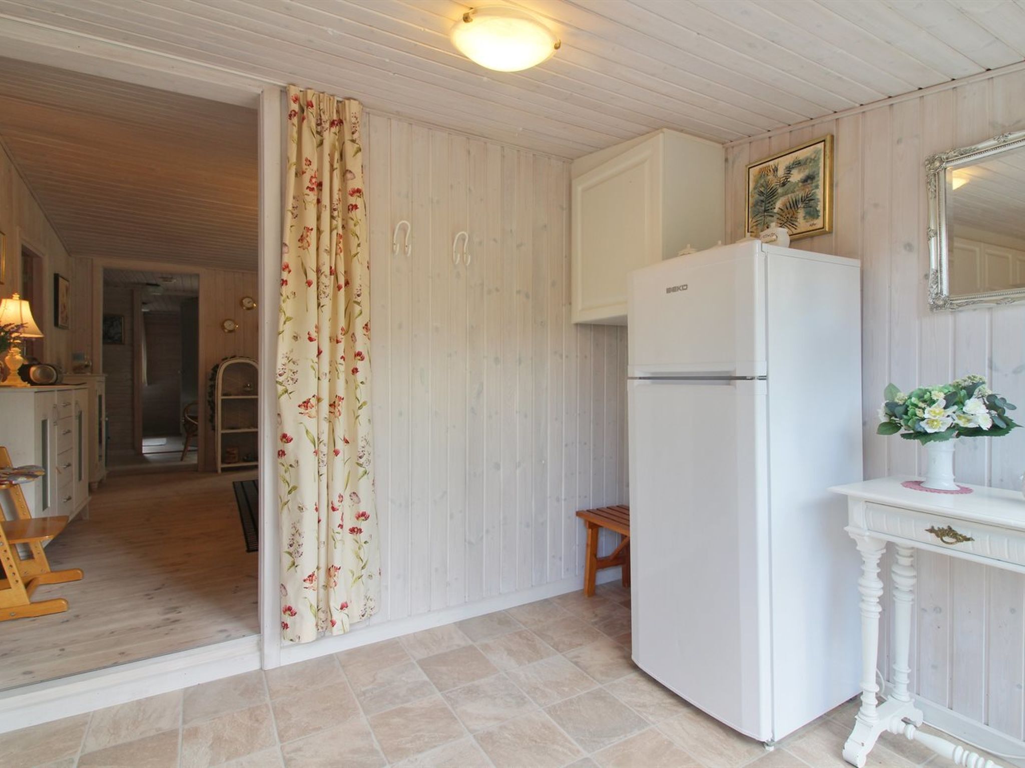 Une cuisine avec un réfrigérateur blanc, des placards en bois, un banc et un rideau à motifs floraux.