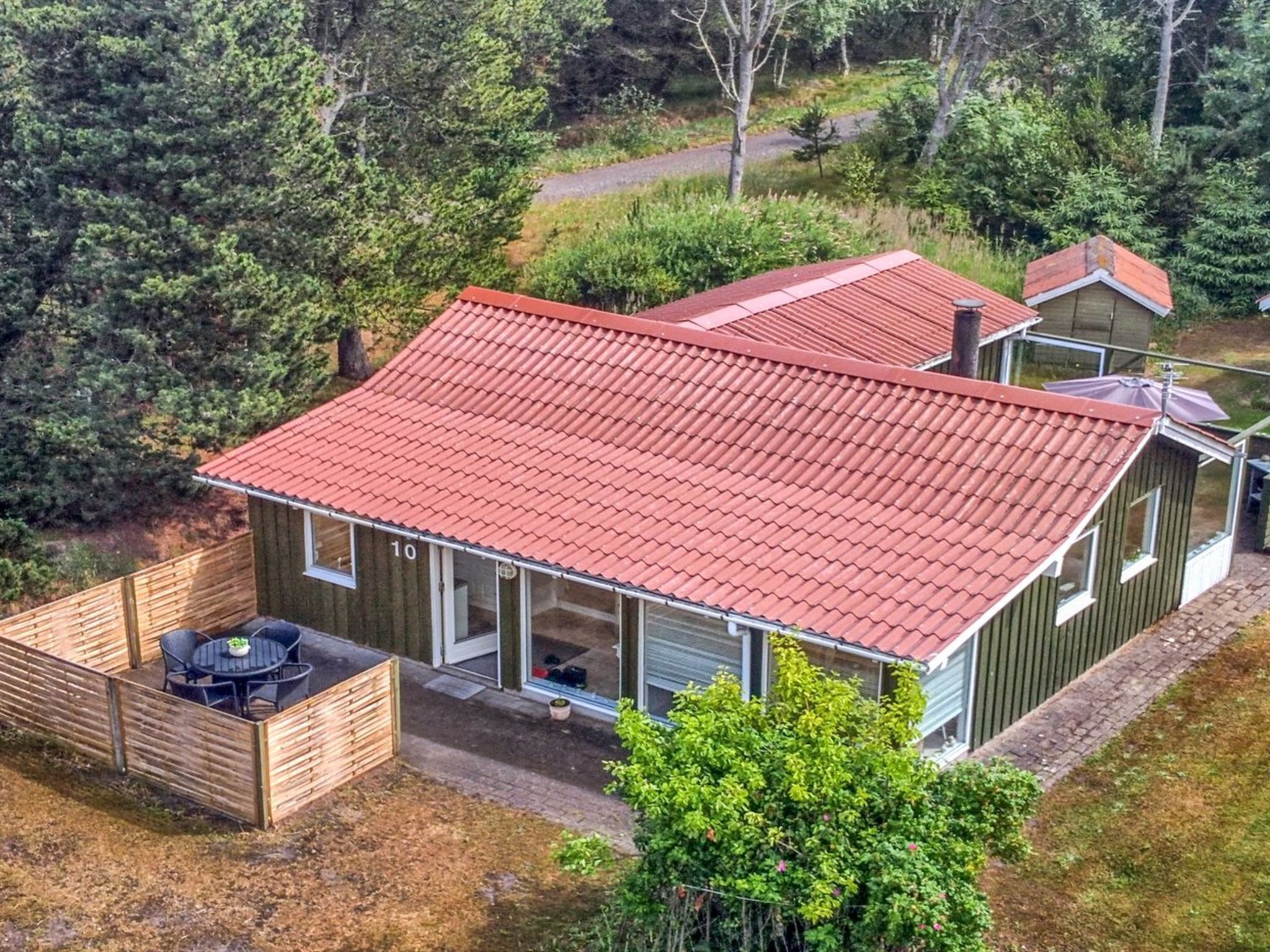 Una casa de dos pisos con techo de tejas rojas, una terraza de madera y un ventanal grande.