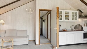 Una stanza accogliente con un divano, un tavolino, angolo cottura con pensili e soffitto in legno.