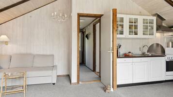 Ein gemütliches Zimmer mit einer Couch, einem kleinen Tisch, einer Küchenzeile mit Schränken und einer Holzbalkendecke.