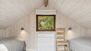 Una camera da letto soffitta accogliente con due letti singoli, una cassettiera in legno e una finestra vista verde.